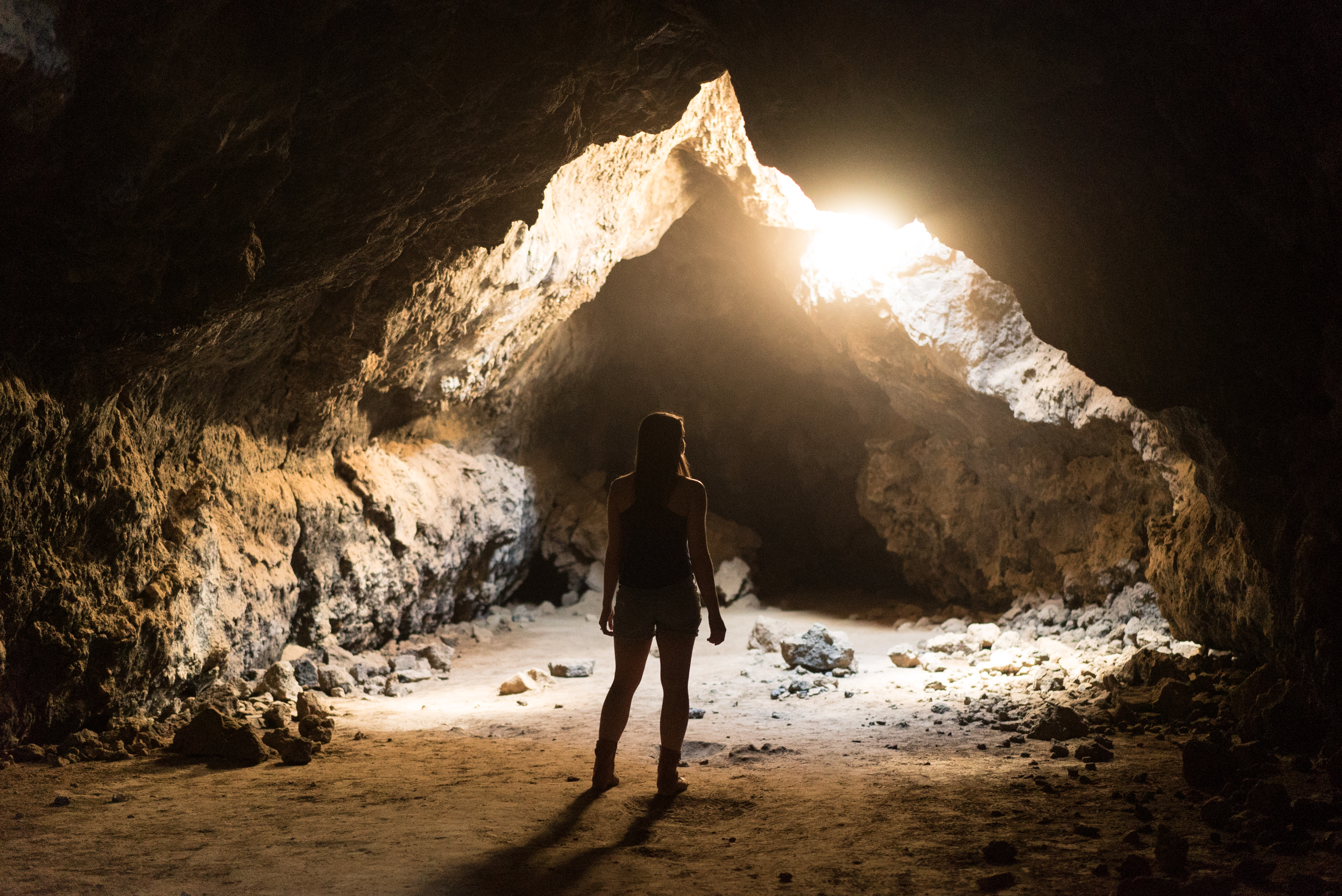 Believing - girl stands looking out of a dark cave toward the light.