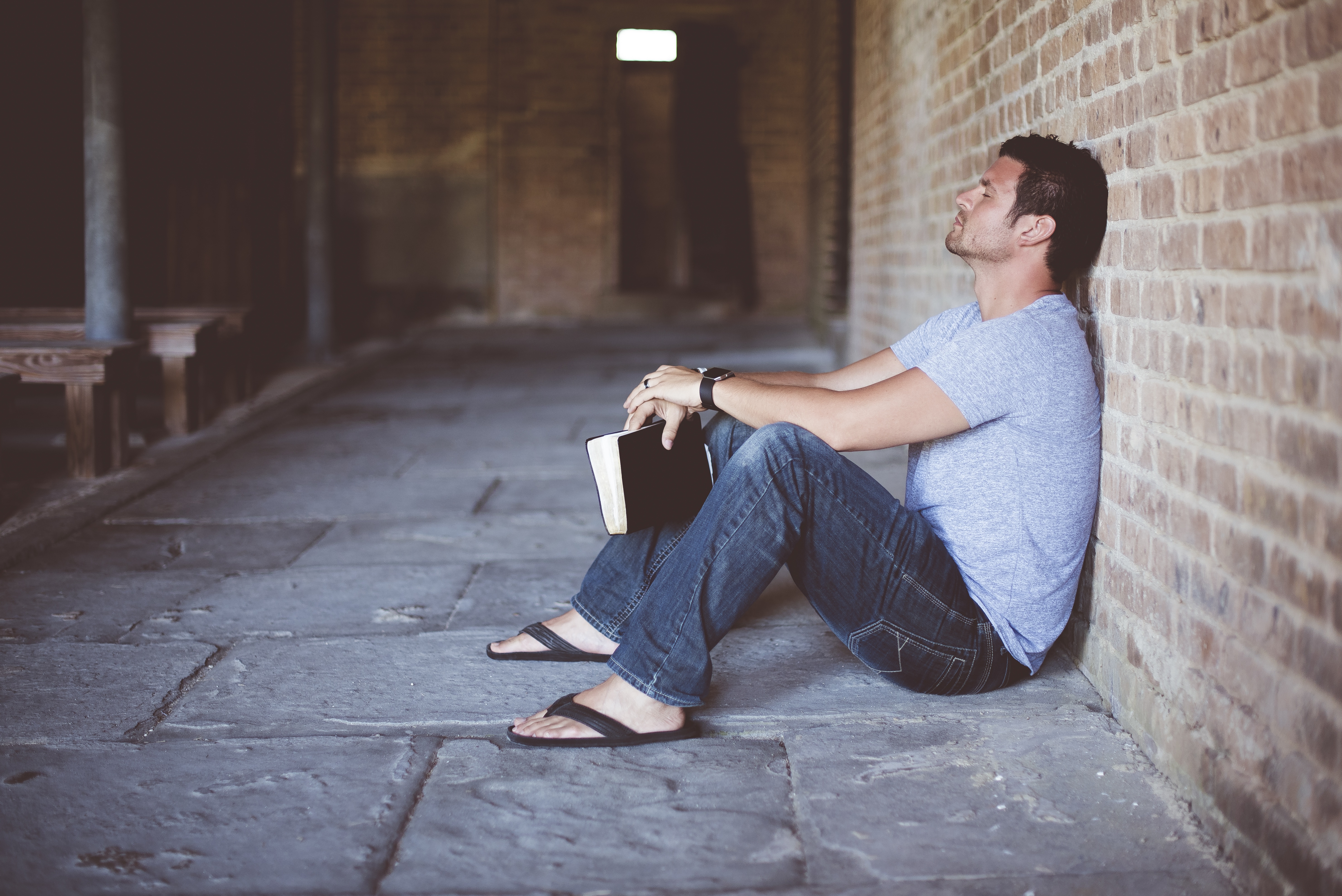 Man sitting on floor holding a Bible - "God has His reasons"...or does He? - Words To The Power